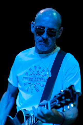 Bald man playing guitar on stage.