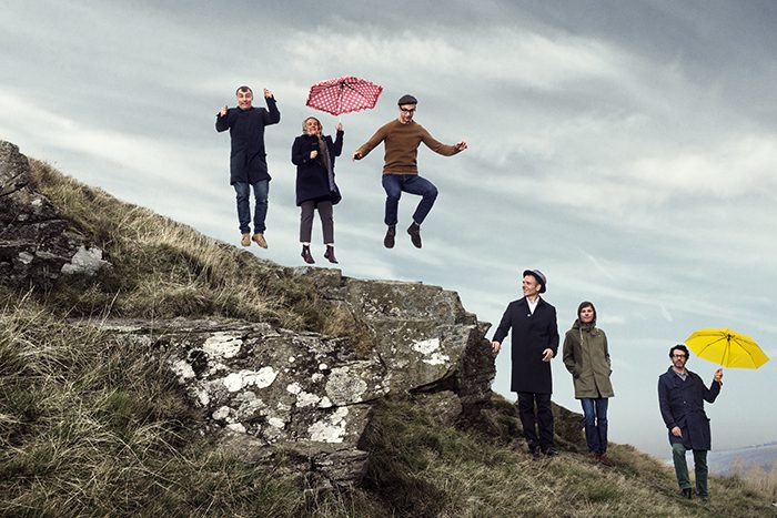 People jumping and walking on grassy hill.