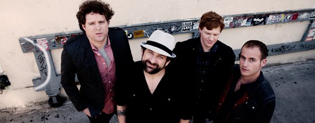 Four men posing outdoors in casual attire.