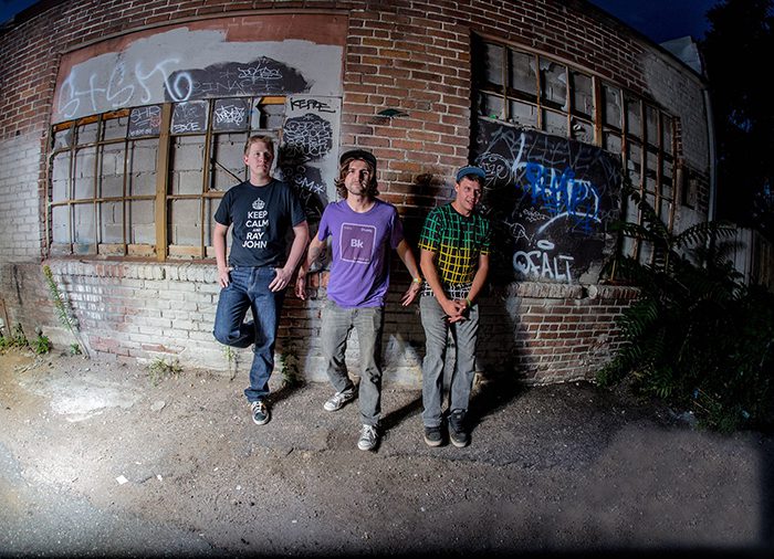 Three people standing by graffiti-covered wall.