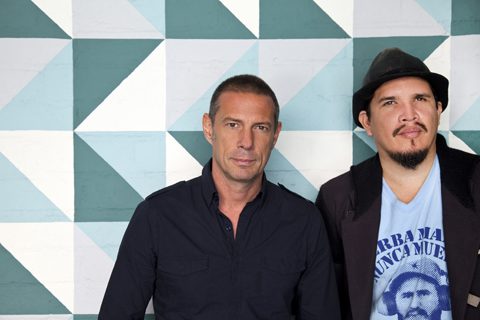 Two men posing against geometric patterned wall.