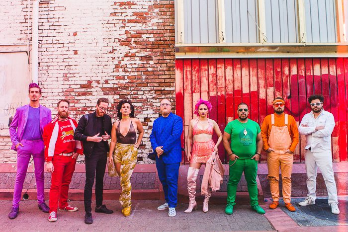 Colorfully dressed group posing against brick wall.