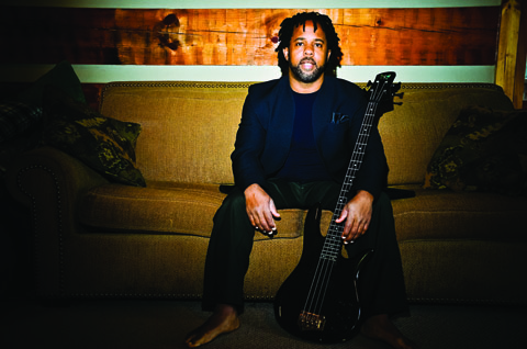 Man sitting on couch with a bass guitar.