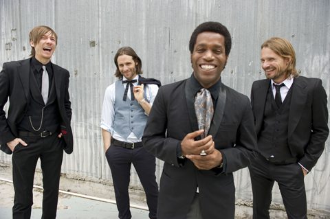 Four men in suits laughing together outdoors.
