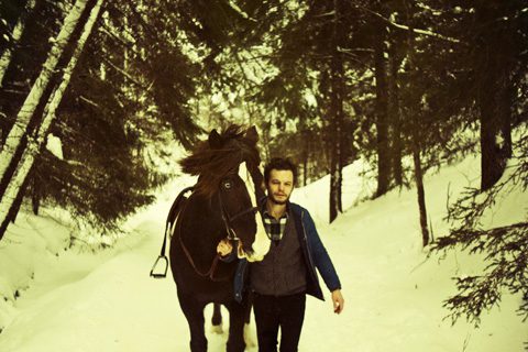 Man walking horse through snowy forest path.