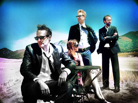 Four people in suits posing outdoors.
