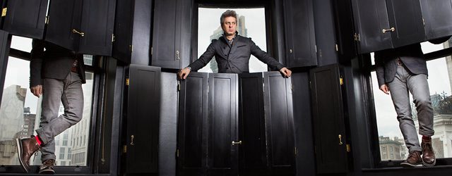 Man standing among black wooden panels.