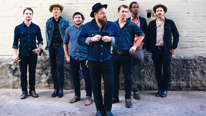 Seven men posing against a brick wall.