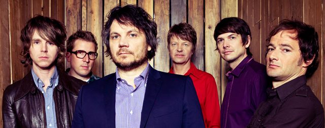 Band members posing in front of wood wall.