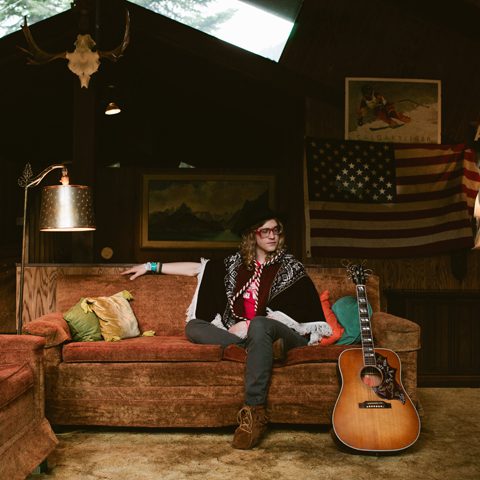 Person sitting on couch with guitar nearby.