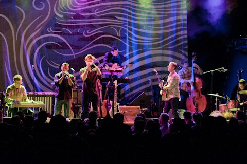 Band performing on stage with colorful backdrop.