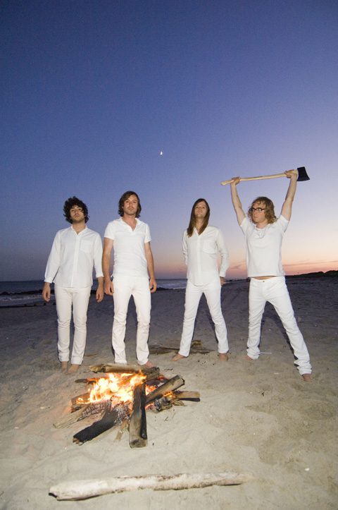 Four people in white by beach bonfire.