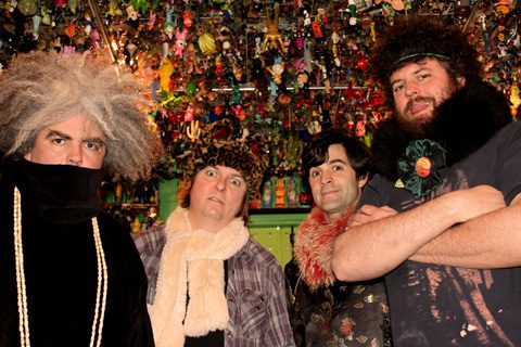 Four people posing in colorful, eclectic setting.