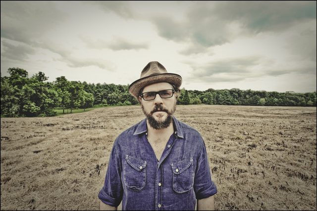 Man in hat standing in dry field.