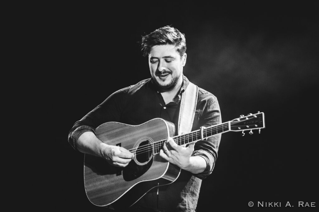 Musician playing acoustic guitar on stage.