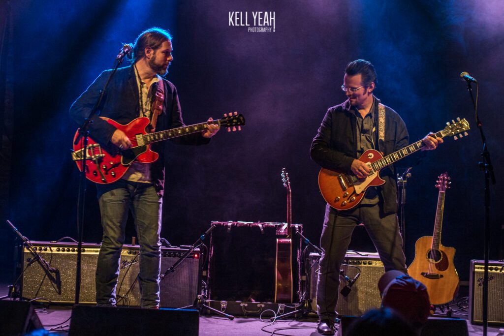 Two musicians playing electric guitars on stage.