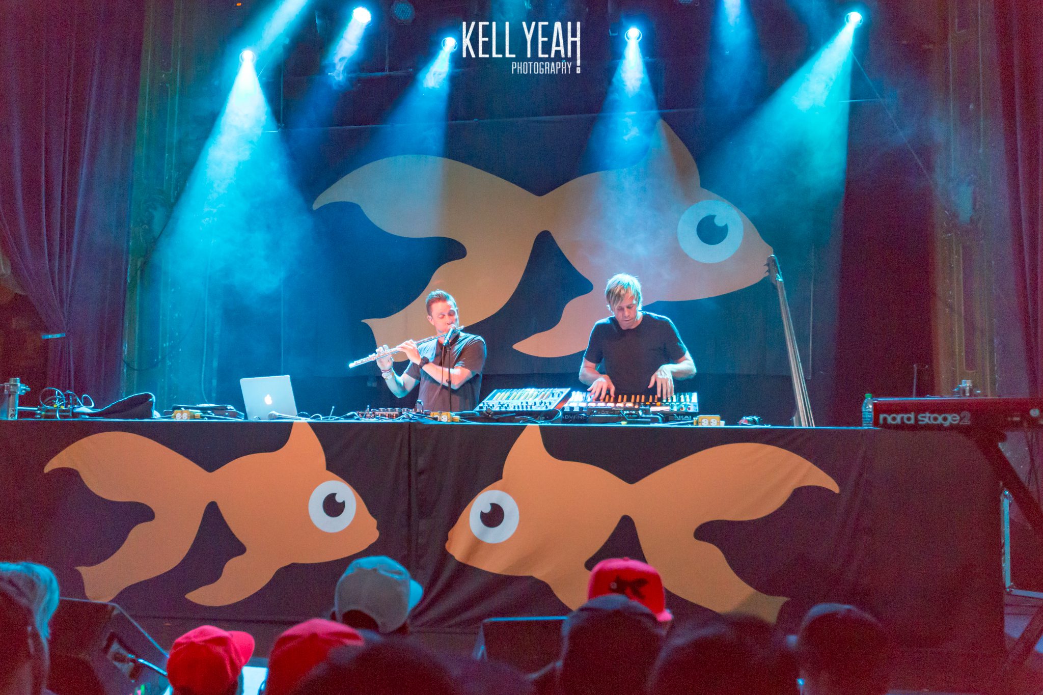 DJs performing on stage with goldfish backdrop.
