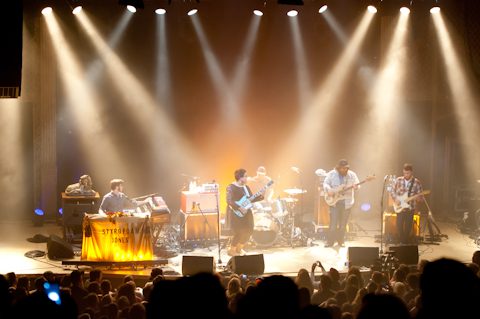 Band performing on stage with bright lights.