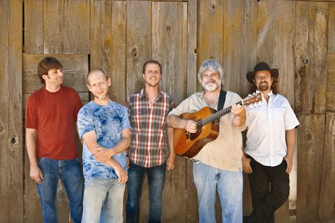 Five men standing with a guitar outdoors.