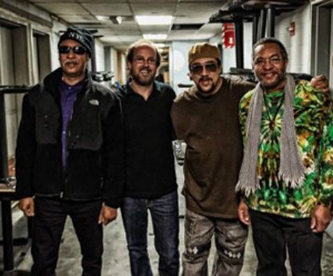 Four men standing together, smiling indoors.