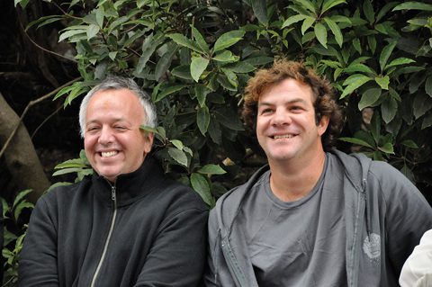 Two smiling men in front of greenery.