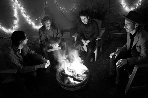 Group sitting around campfire with string lights.