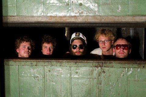 Five men peeking through a metal opening.