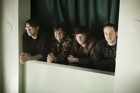 Four men leaning on a green ledge.