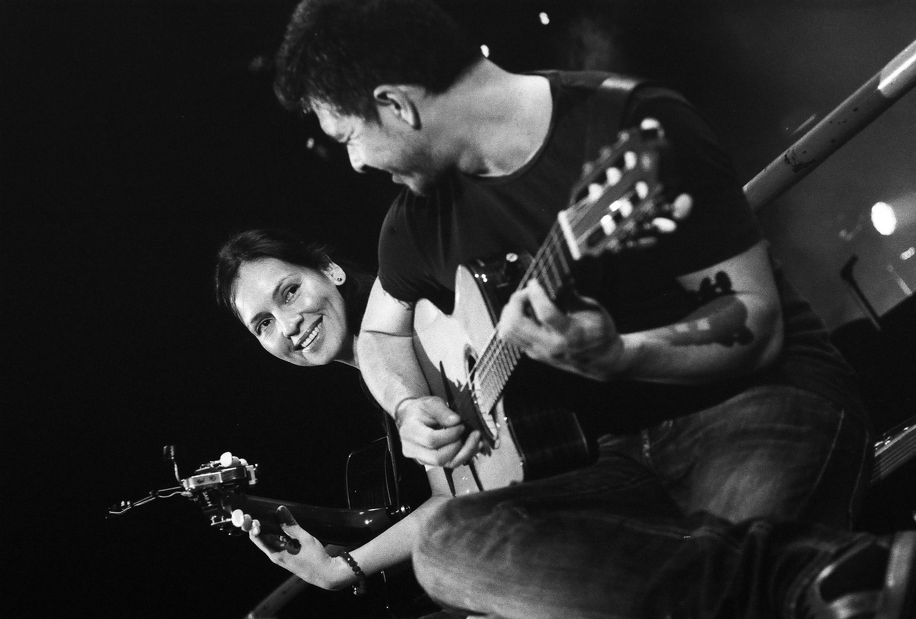 Two people playing guitars, smiling together.