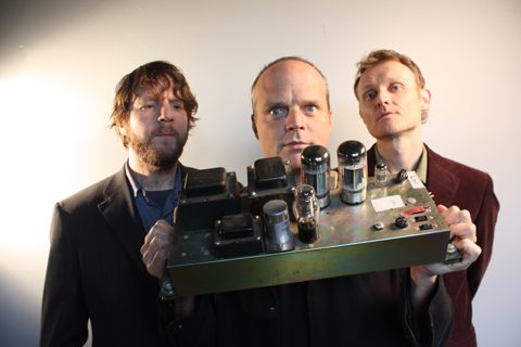 Three men holding a vintage electronic device.