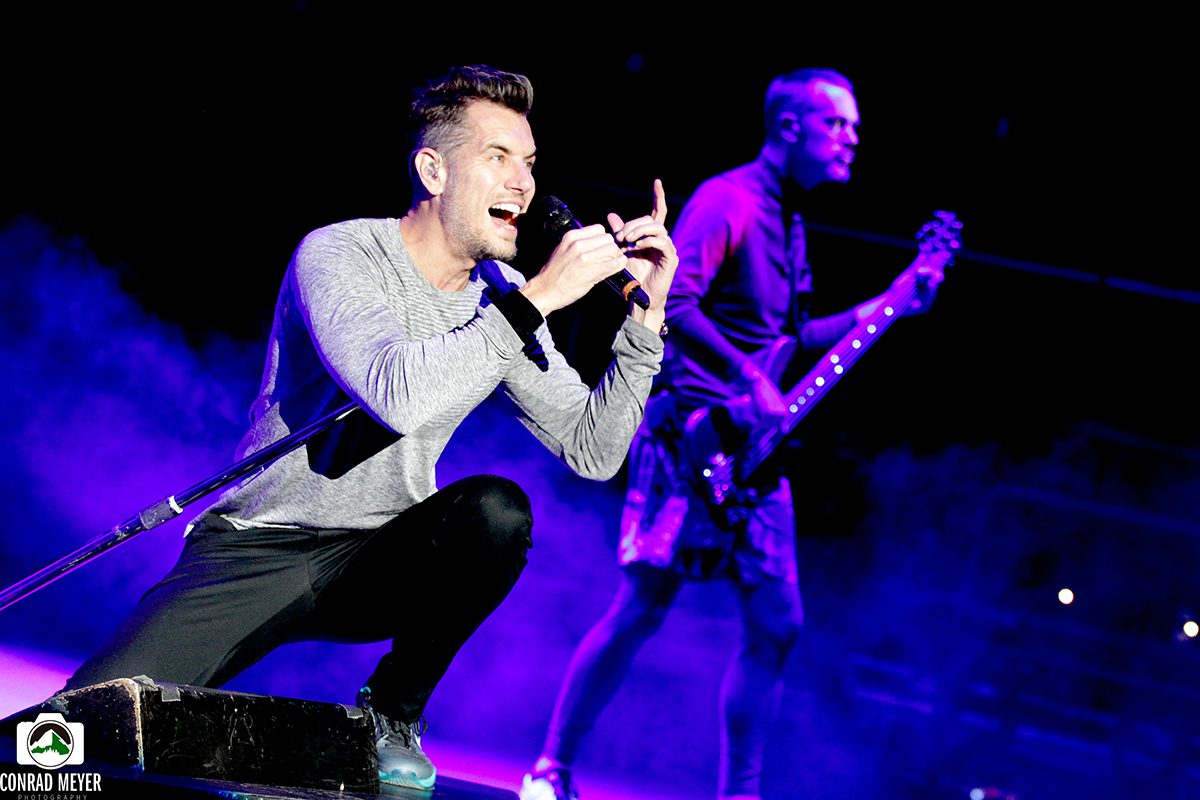 Singer performing energetically on stage with guitarist.