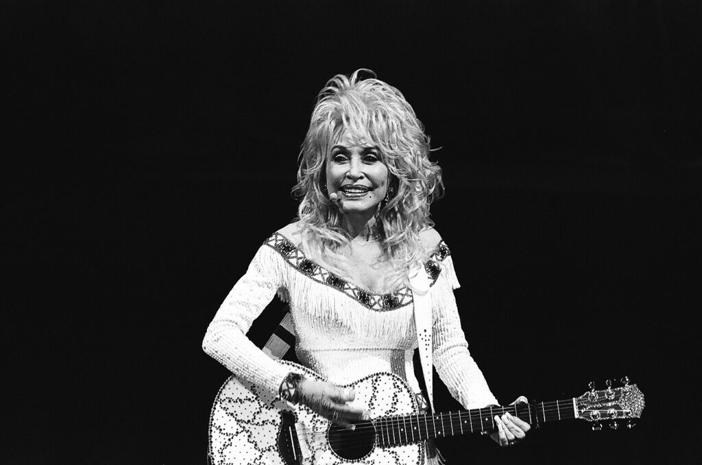 Singer playing guitar on stage, smiling joyfully.