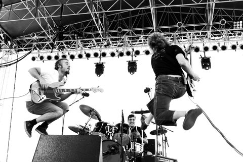 Band performing energetically on stage, musicians jumping.