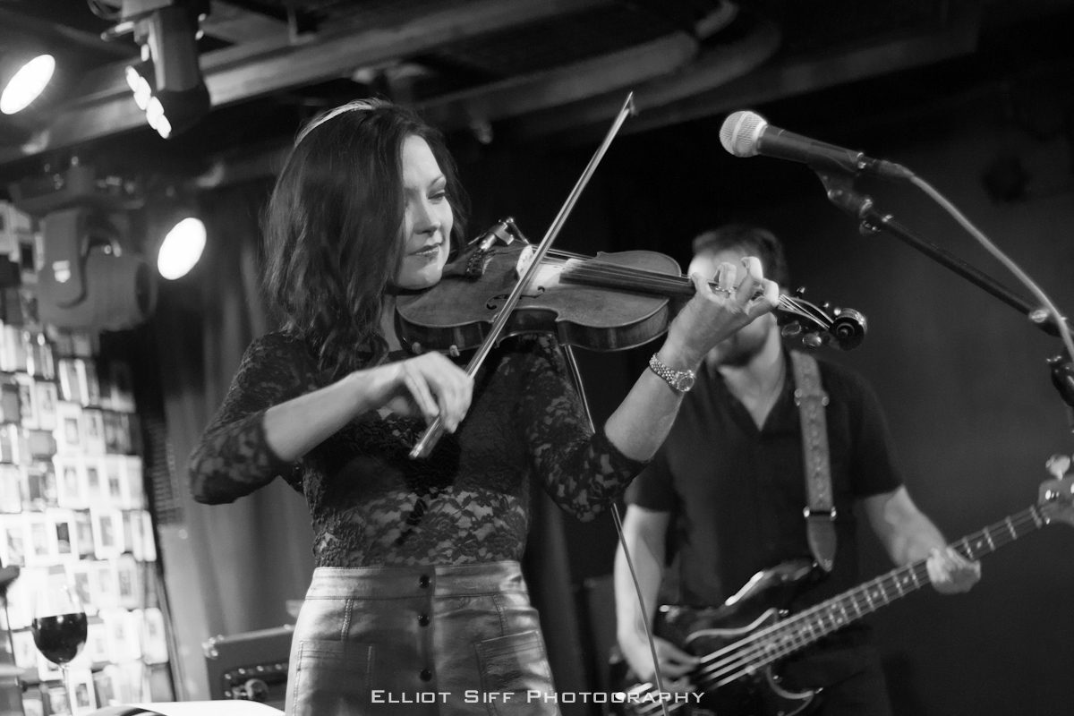 Woman playing violin on stage with band.