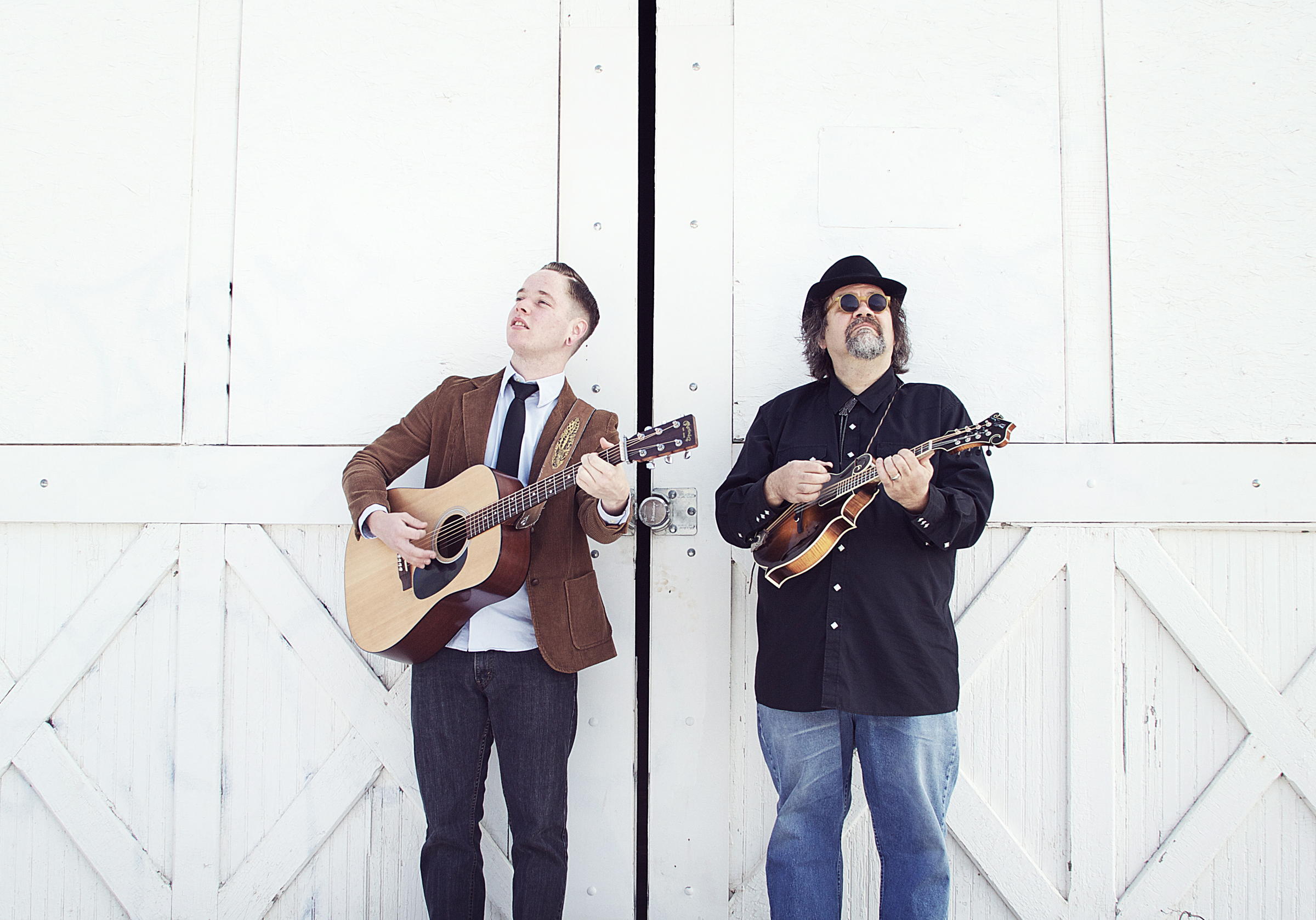 Two musicians playing guitars against white doors.