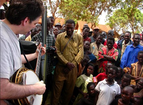 Musician playing banjo for gathered crowd outdoors.