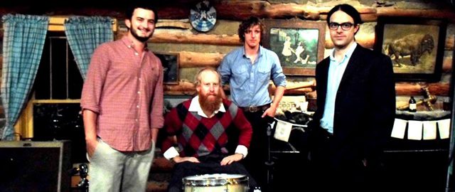 Four men posing in a rustic room.