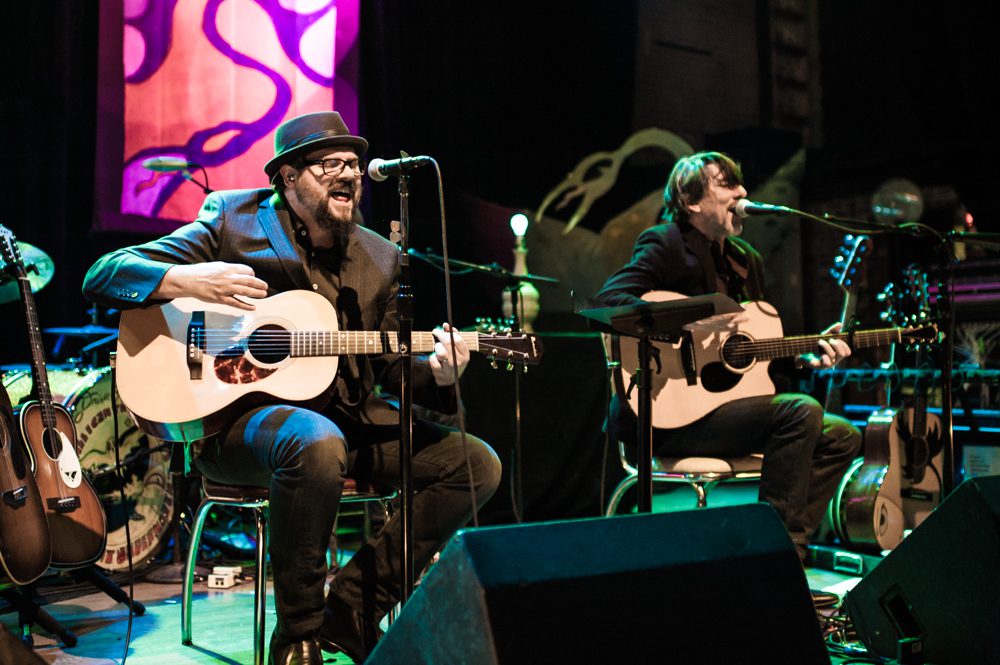 Musicians performing with acoustic guitars on stage.