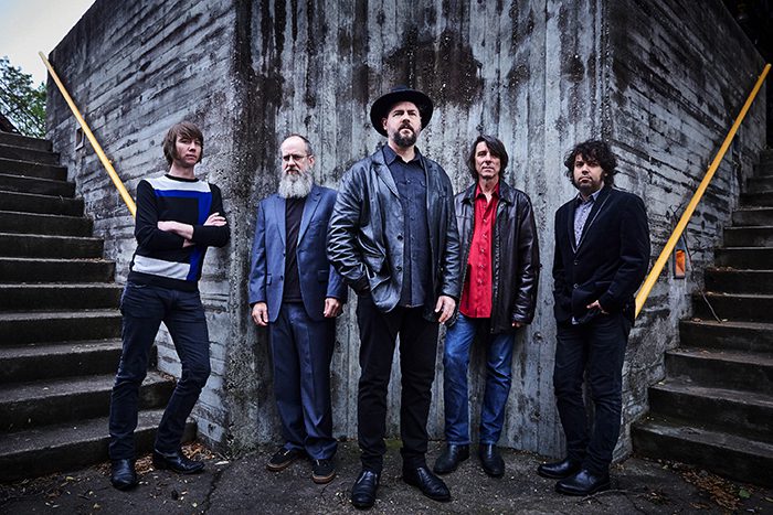 Five men standing against concrete wall.