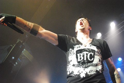 Singer performing energetically on stage with microphone.