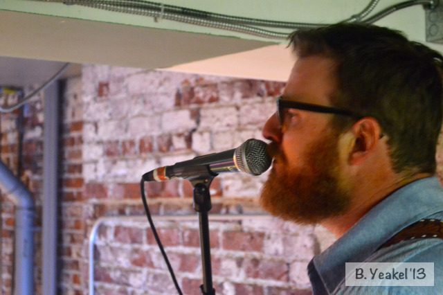 Man singing into microphone, brick wall background.