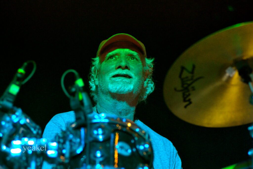 Drummer performing under green stage lights.
