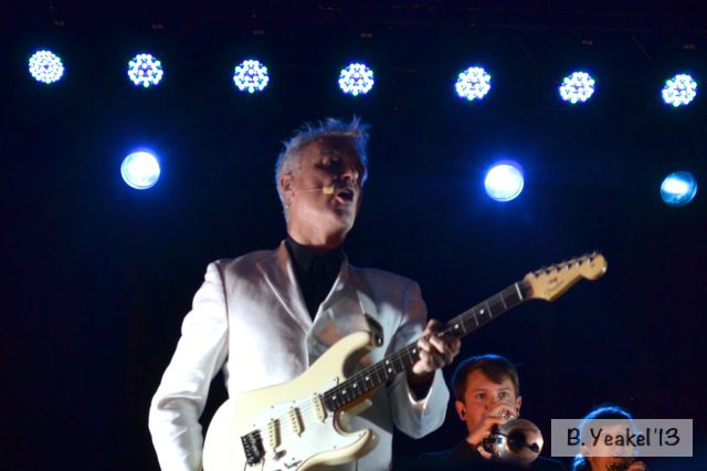 Musician playing guitar under stage lights.
