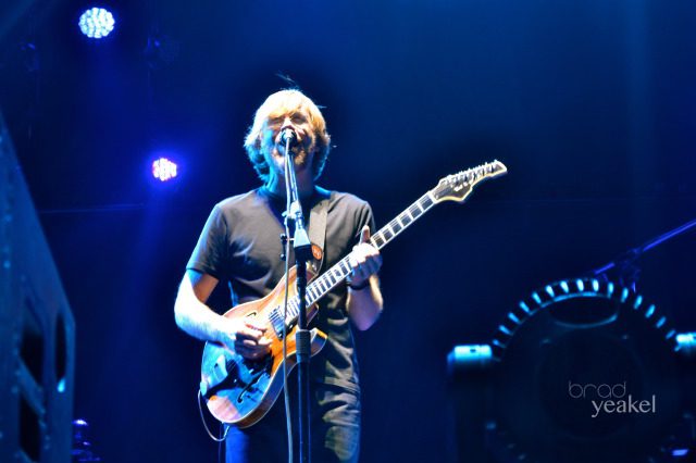 Guitarist performing on stage under blue lights.