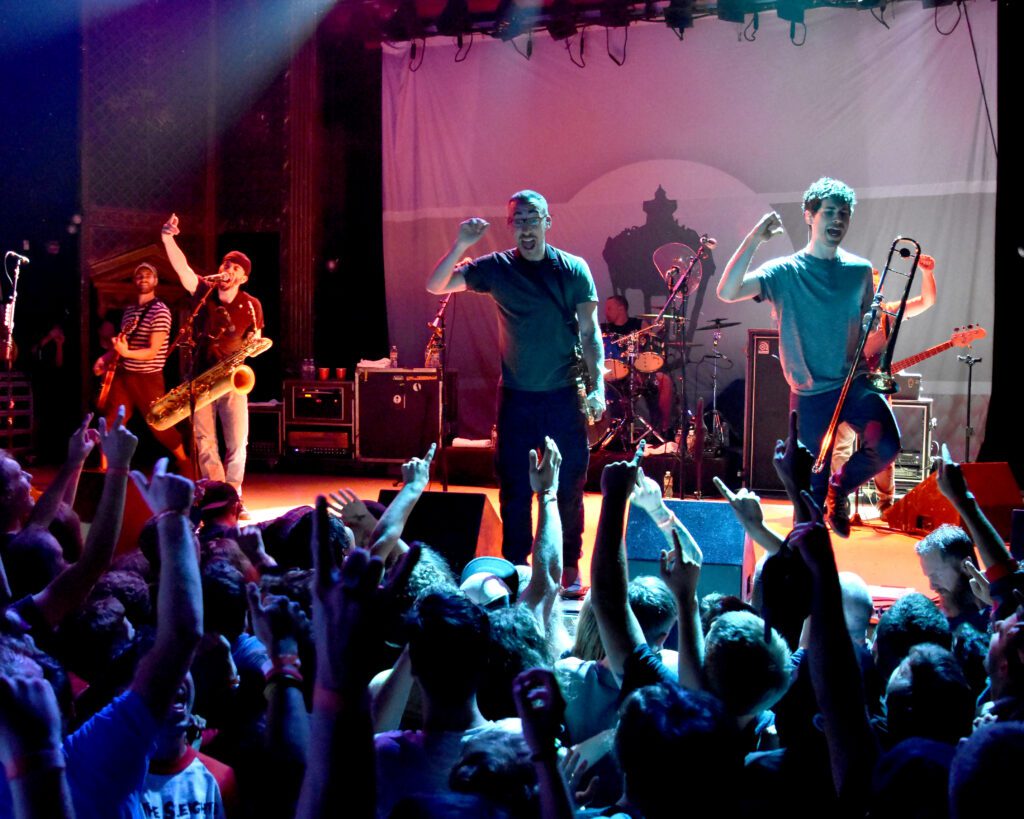 Band performing energetically on stage with audience.