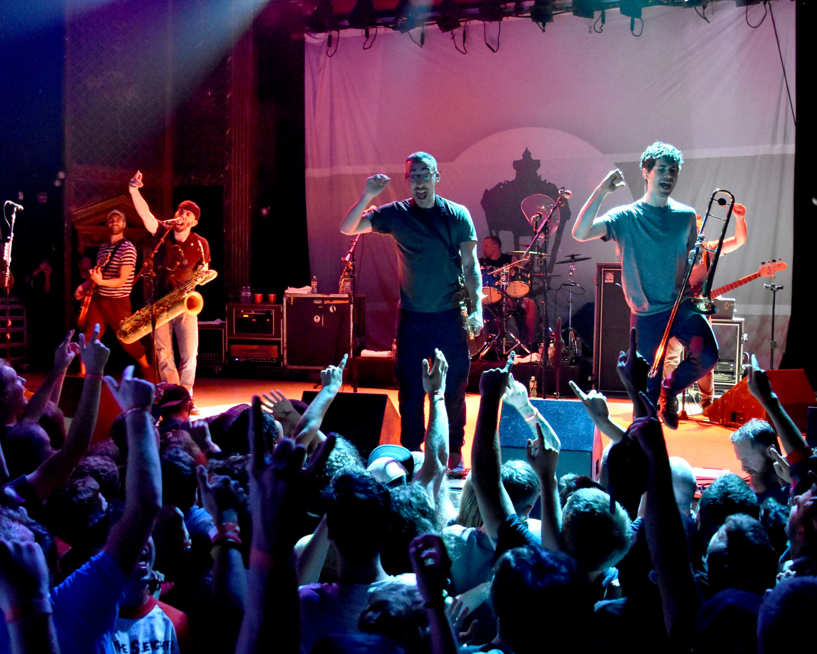 Band performing energetically on stage with audience.