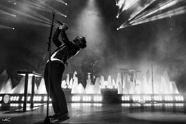 Singer performing on stage with dramatic lighting.