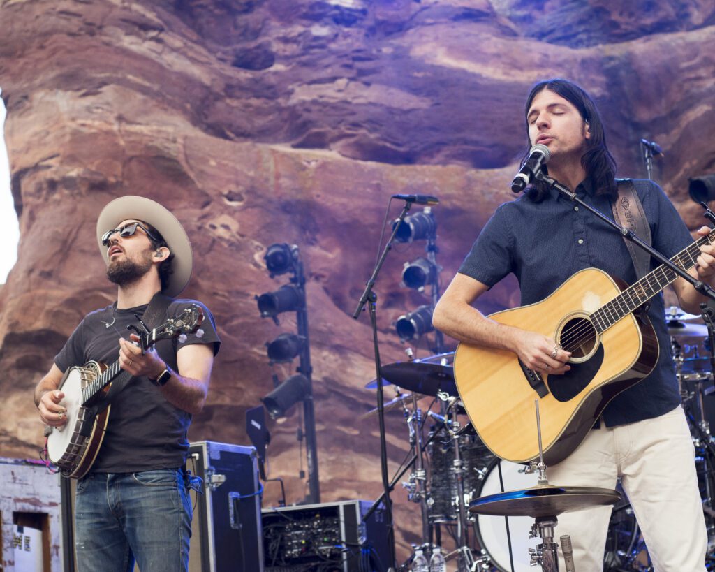 Musicians performing with guitars on outdoor stage.