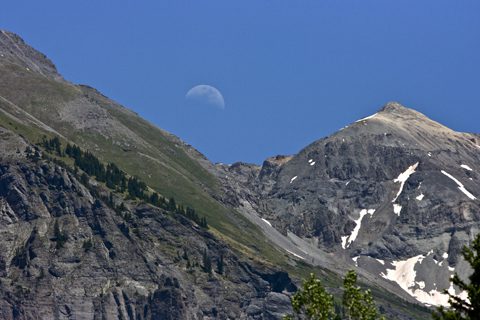 Moon over rugged mountain peaks, clear sky.