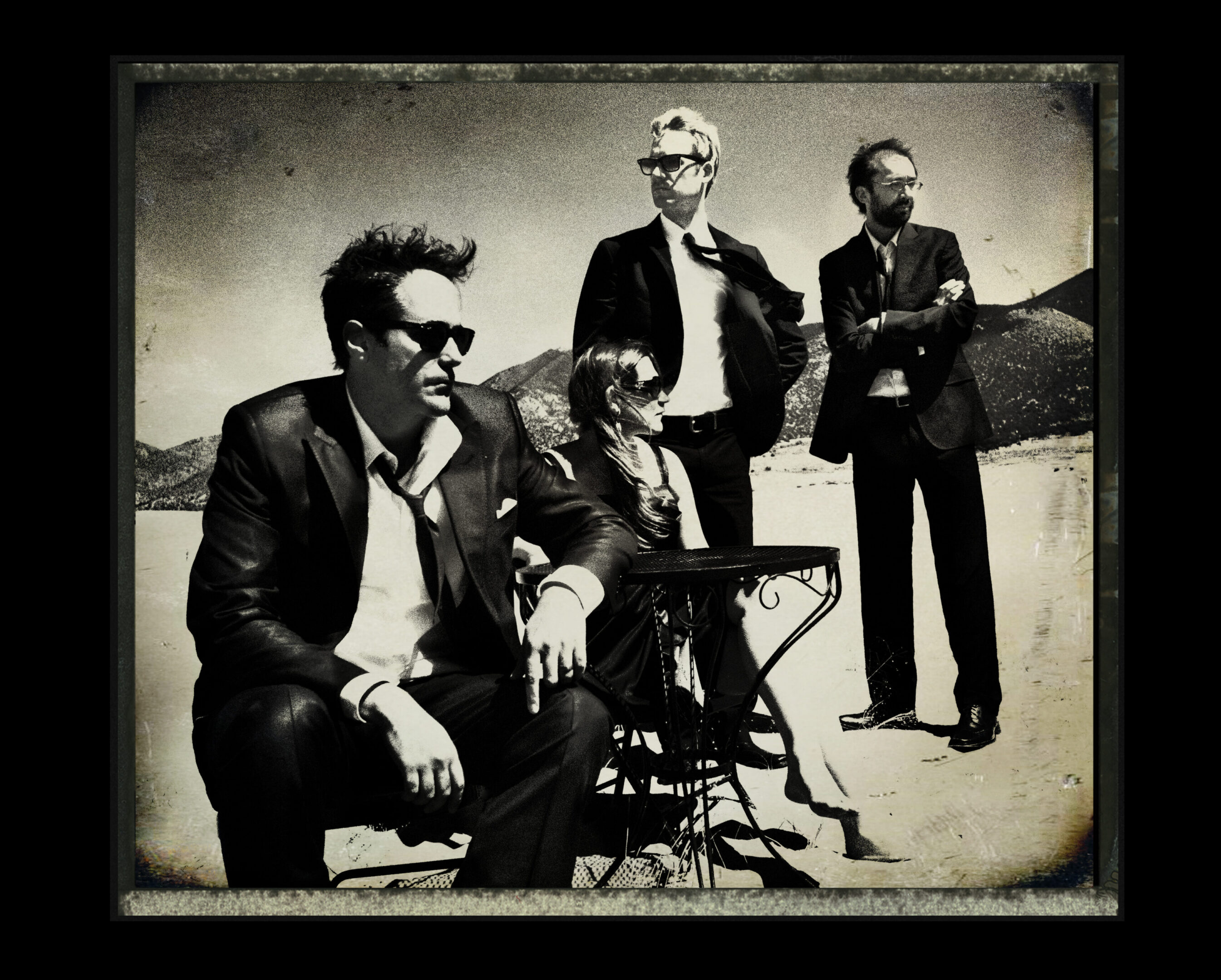 Four people in suits, outdoors, vintage style.